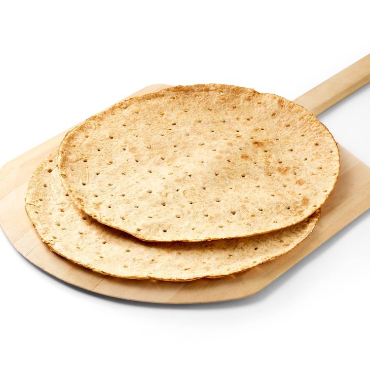 Two round, thin, light brown colored pizza crusts with small holes, placed on a wooden pizza peel.