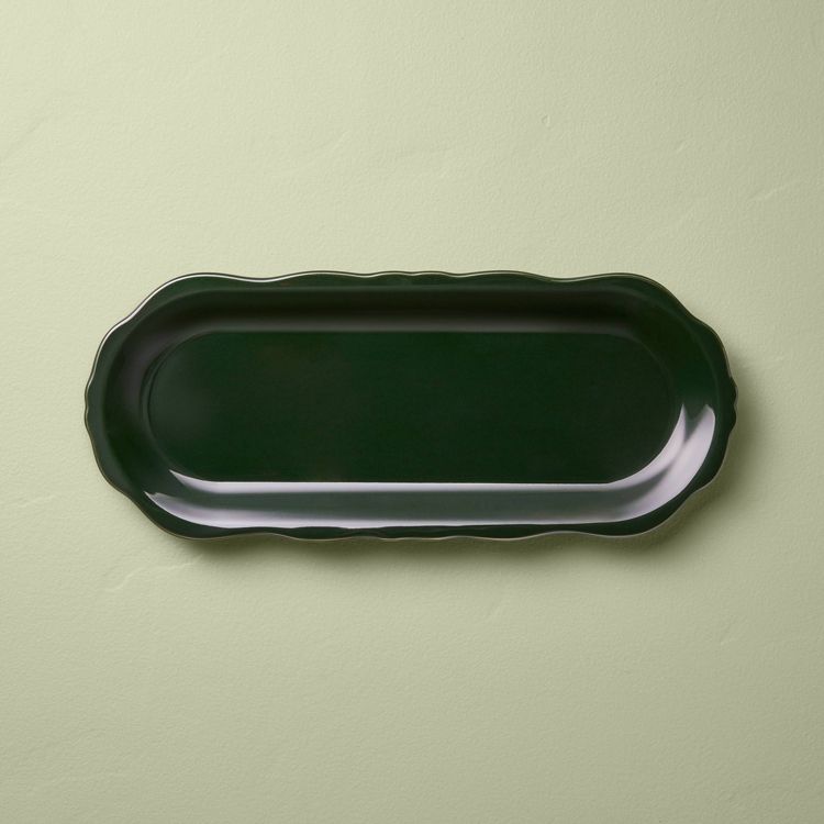 A dark green colored, oval-shaped tray with a scalloped edge placed on a light green surface.