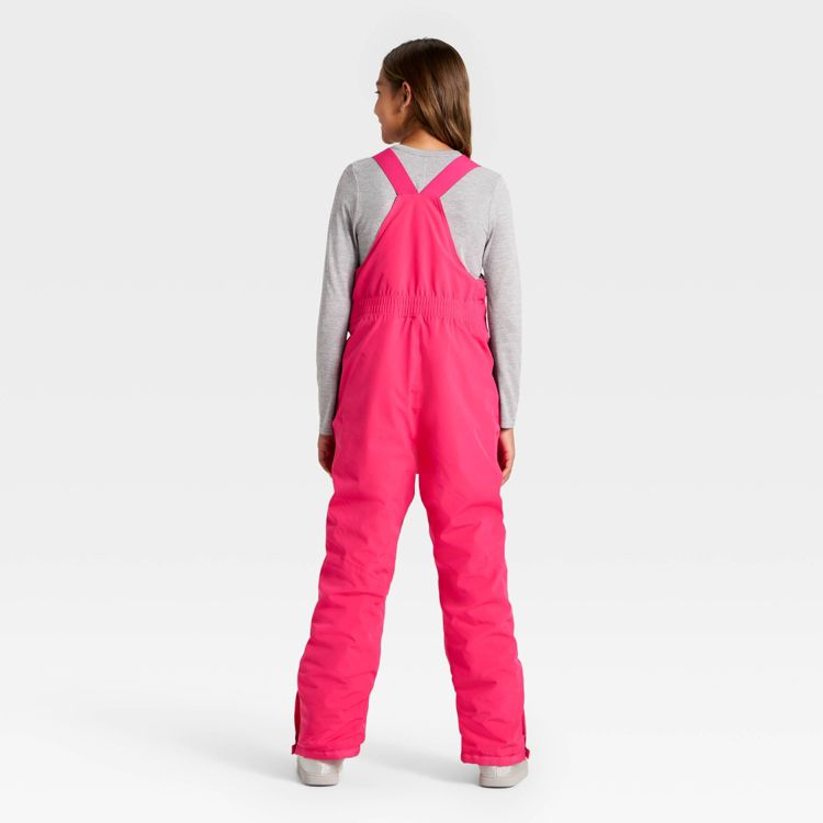 Bright pink colored bib-style snow pants with adjustable shoulder straps and elastic waistband, shown from the back.
