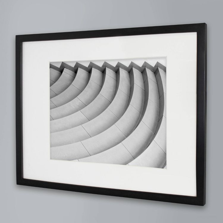A black colored frame with a black and white photo of curved architectural steps against a gray wall.