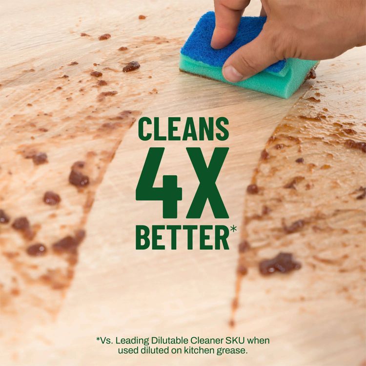 A hand uses a blue and green sponge to clean a wooden surface with text reading "CLEANS 4X BETTER*" and a note below.