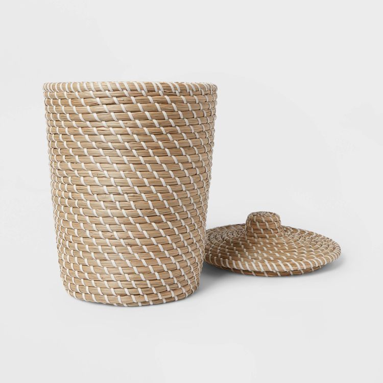A woven tan and white colored wastebasket with a matching lid placed beside it.
