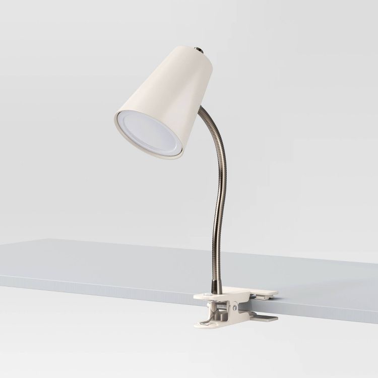 A white colored clamp lamp with a flexible neck attached to the edge of a light gray surface.