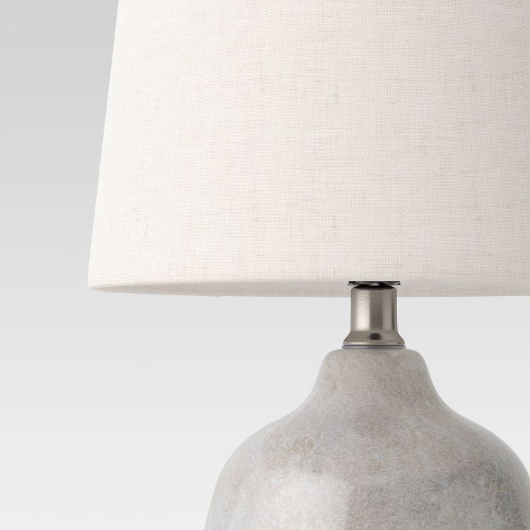 A table lamp with a light gray colored textured base and a white colored fabric shade.