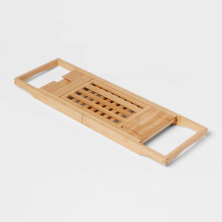 A wooden bath caddy with slatted design and handles on each end.