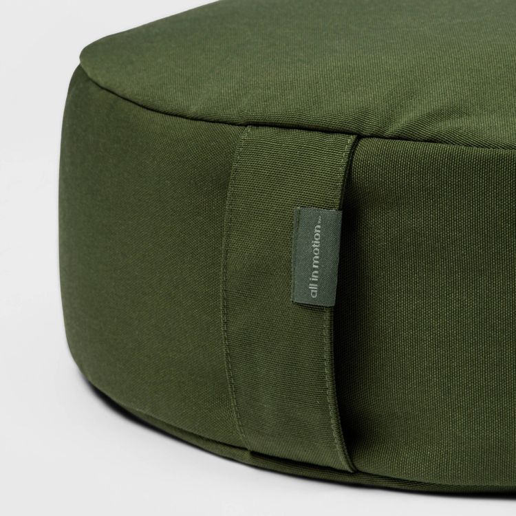 Round green colored pillow with a fabric handle and a tag reading "all in motion."