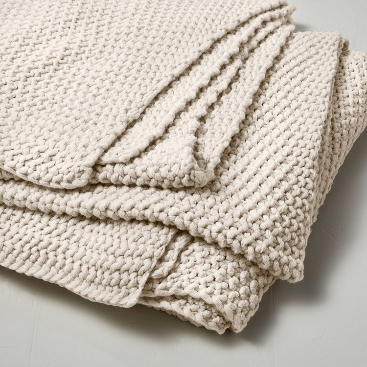A natural-colored chunky knit bed blanket with a textured pattern, folded neatly.