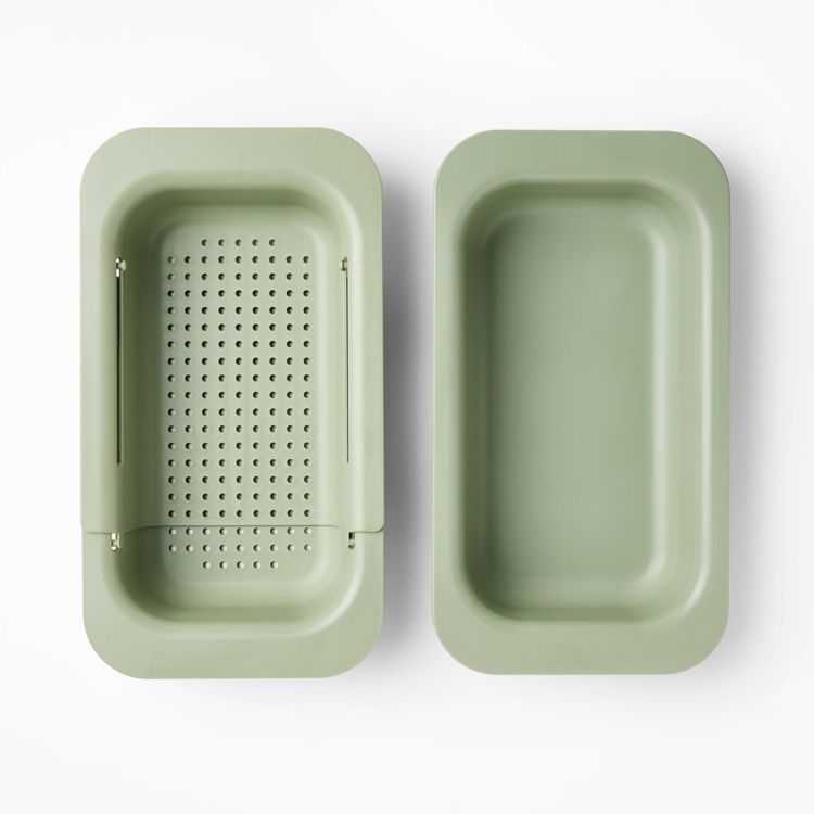 A green colored rectangular colander with perforations next to a matching solid tray.